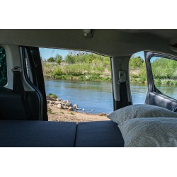Cozy kombivan interior with an unfolded bed and pillows, overlooking a beach and a river