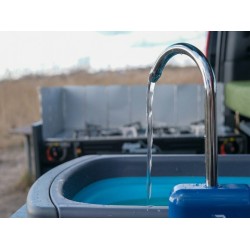 Close-up of water flowing from the tap and the operating gas stove with a wind shield in the background