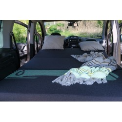 Cozy interior arrangement of a Vacamod micro-camper with an unfolded bed, grey foam mattresses, pillows, and a blanket
