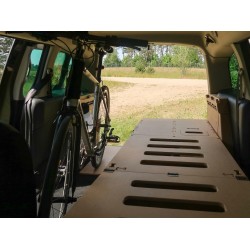 Unfolded single bed Vacamod KombiVan SOLO PREMIUM without a mattress next to a bicycle inside a van.