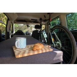 Long single bed Vacamod SOLO with a grey mattress, breakfast board, and a bicycle packed into the car in the background.