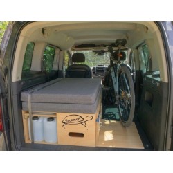 Spakowany campingbox Vacamod SOLO PREMIUM po lewej stronie bagażnika z szarymi materacami i pasem.