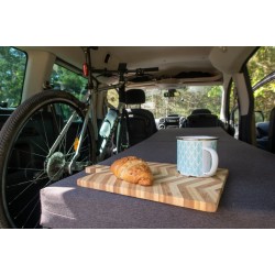 Mattress-level view of a long Vacamod SOLO BASIC bed on the right side, breakfast tray, and a bicycle.