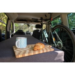Grey mattress-level view of a long Vacamod SOLO BASIC bed on the left side, breakfast tray, and a bike.